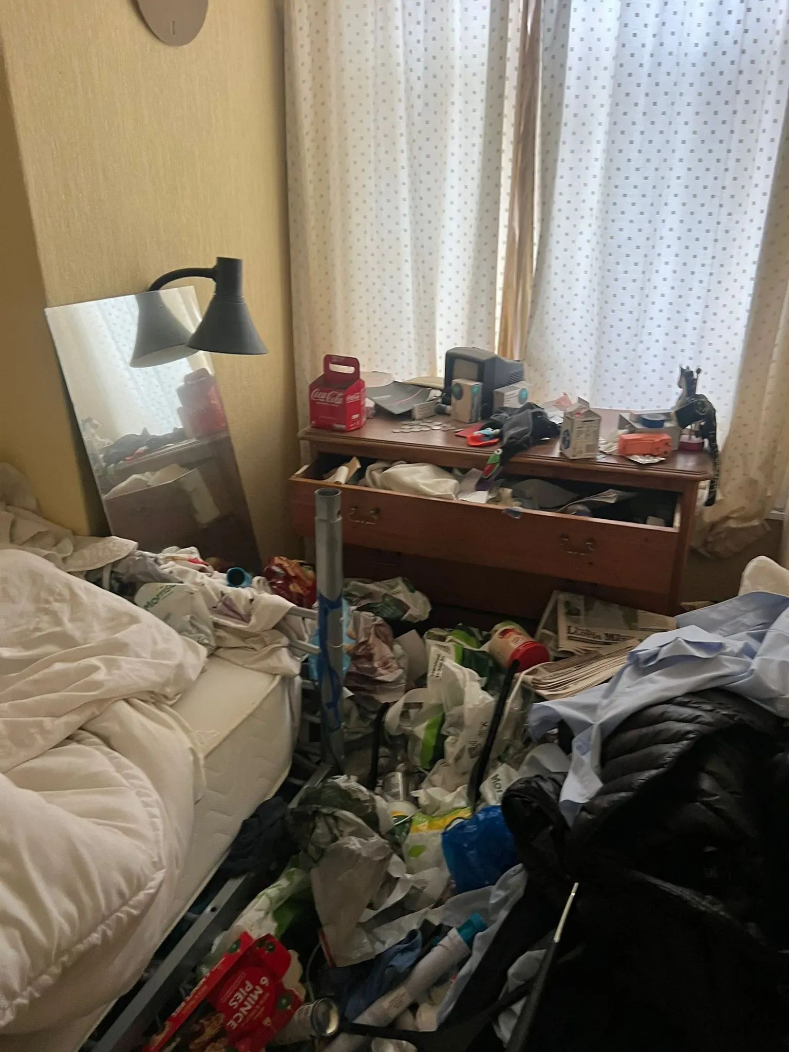 A highly cluttered bedroom in need of a professional hoarder clearance service, showing extensive rubbish and items on the floor and furniture.